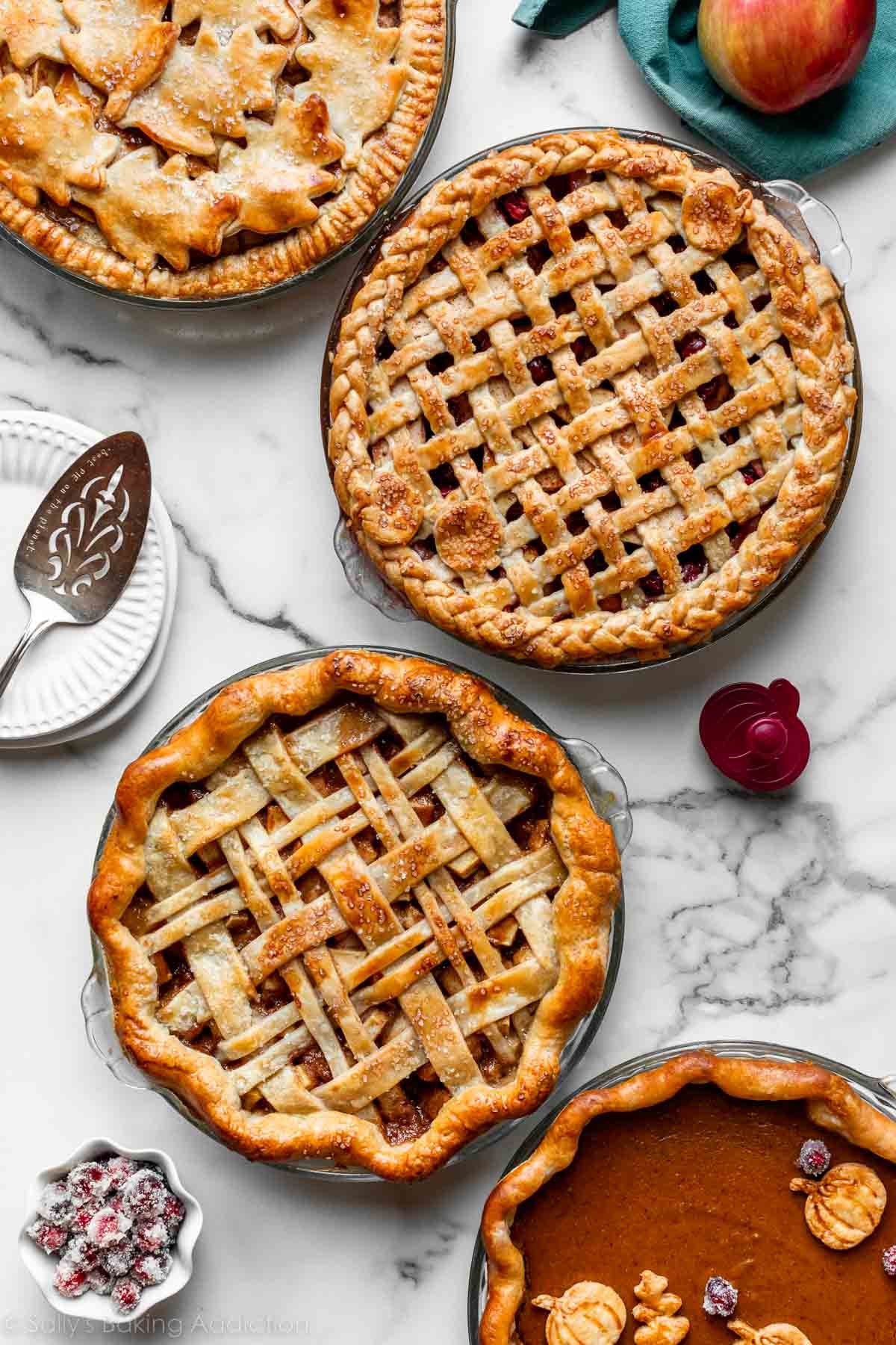 4 baked pies with different pie crust designs on marble counter.