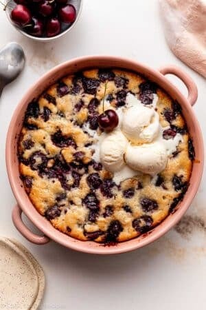 cherry cobbler in pink ceramic baking dish.