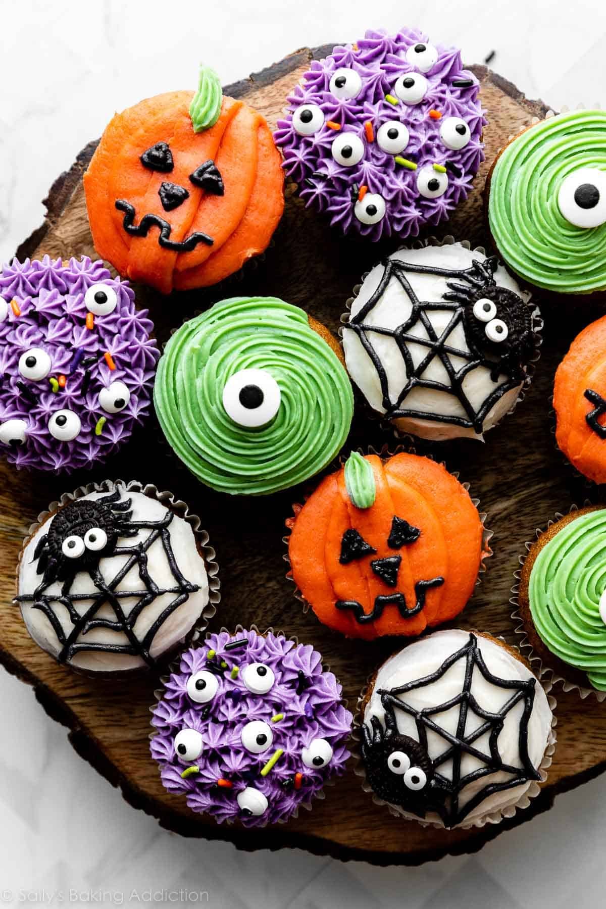 decorated Halloween cupcakes including purple monsters, green monsters, spiders and spider webs, and pumpkin Jack-O-Lanterns.