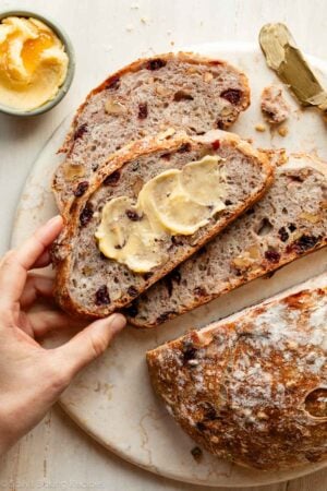 hand grabbing slice of buttered cranberry nut bread.