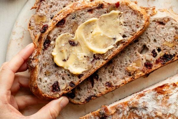 hand grabbing slice of buttered cranberry nut bread.