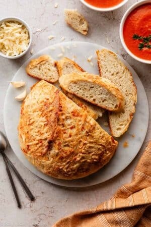 asiago cheese-crusted bread on marble cutting board with 2 bowls of tomato soup.