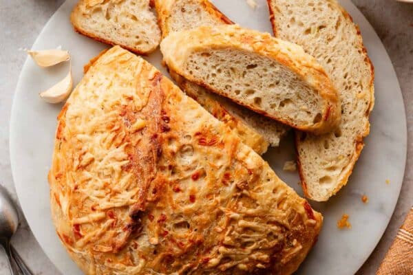 asiago cheese-crusted bread on marble cutting board with 2 bowls of tomato soup.