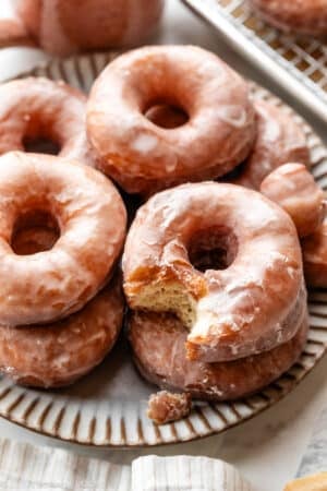 doughnuts piled on gray plate with one with bite taken out.