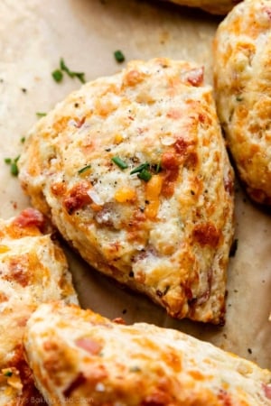 ham and cheddar cheese scone with chives and sea salt garnish on top sitting on brown parchment paper.