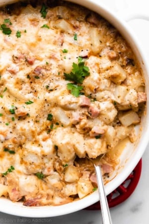 cheesy ham and potato casserole in white dish with serving spoon sitting in it.