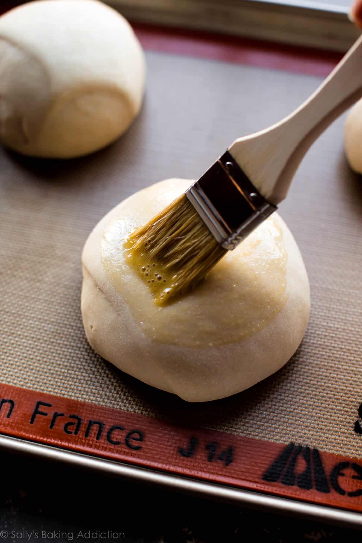 brushing egg wash onto bread bowls dough before baking