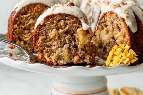 slice of hummingbird Bundt cake with icing and yellow flowers on cake stand.