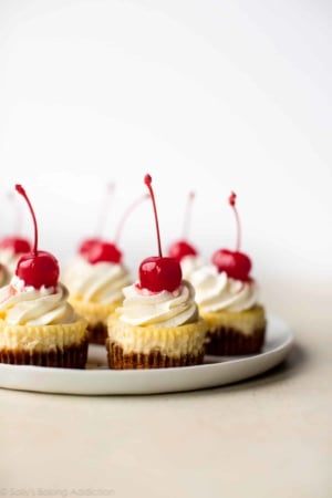 mini cheesecakes with whipped cream and cherries on top on a white plate