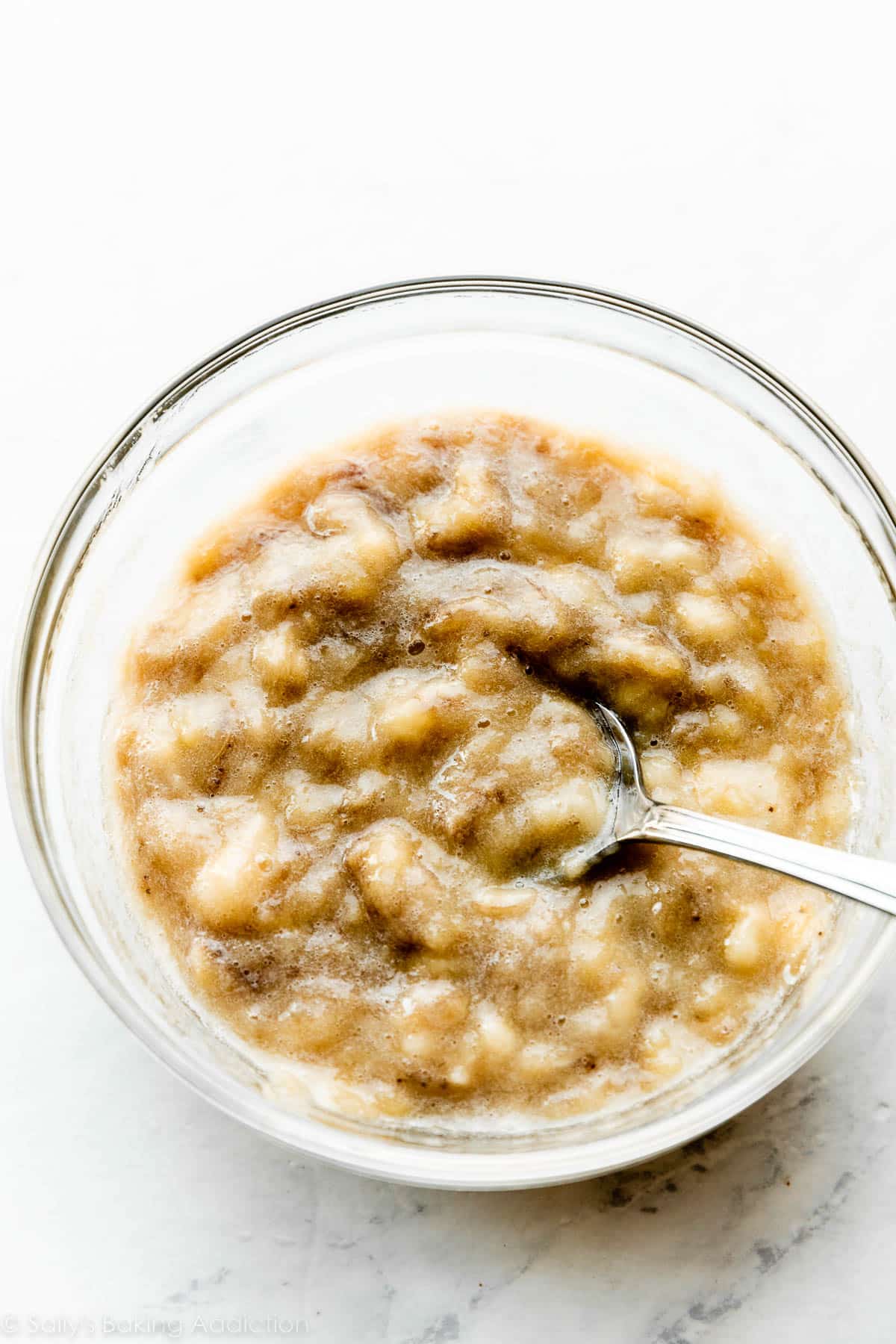 mashed bananas in glass bowl with spoon.