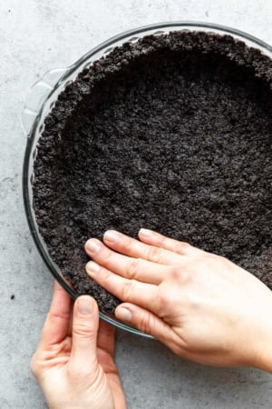 two hands pressing Oreo cookie crust into pie dish.