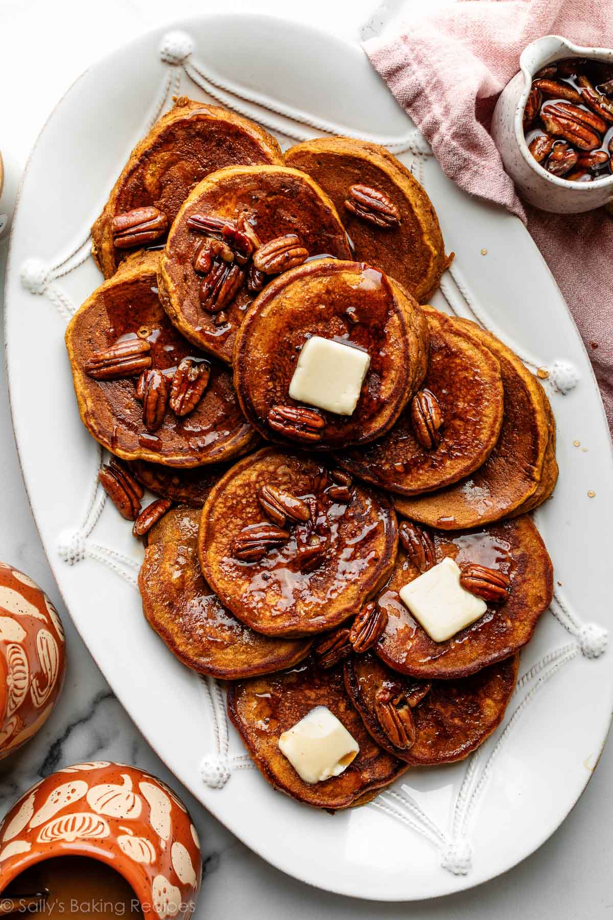 pumpkin pancakes with slices of butter and maple pecan syrup on top sitting on white platter.