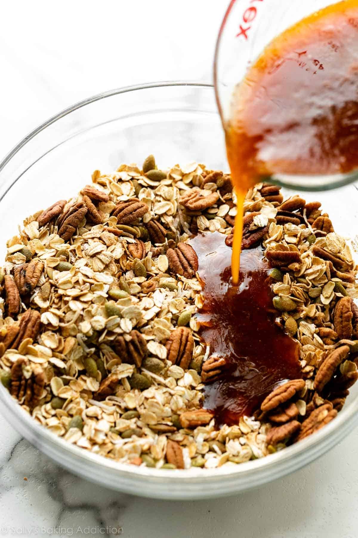 pouring pumpkin liquid wet ingredients on bowl of oats, pumpkin seeds, and pecans.