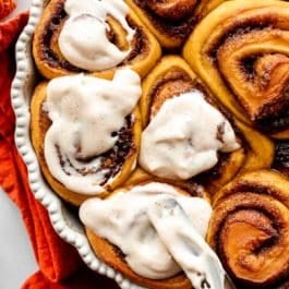 spreading icing on warm pumpkin cinnamon rolls