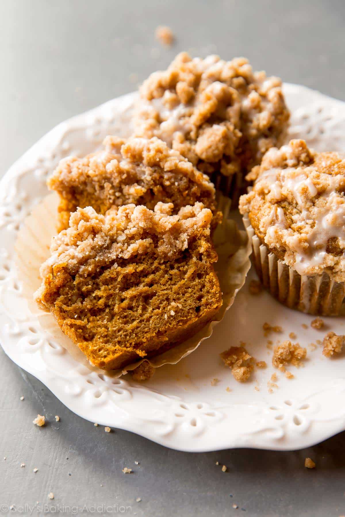 pumpkin crumb cake muffins on a white plate with a muffin cut in half showing the inside