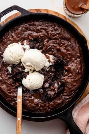 skillet brownie in cast iron skillet with vanilla ice cream and caramel sauce.